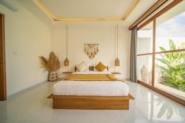 Sleep with a view – This serene bedroom with glass walls offers breathtaking views of the lush garden and private pool, creating a peaceful retreat in your luxury Bali villa.