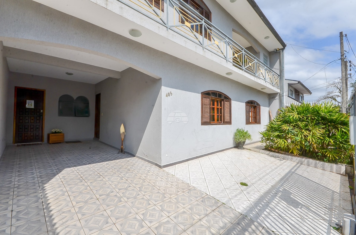 The exterior of the house features a spacious entryway adorned with decorative tiles and a well-maintained garden. Large windows invite natural light, while a covered area provides shelter. The balcony above is accessible through wooden doors, promoting a sense of openness.