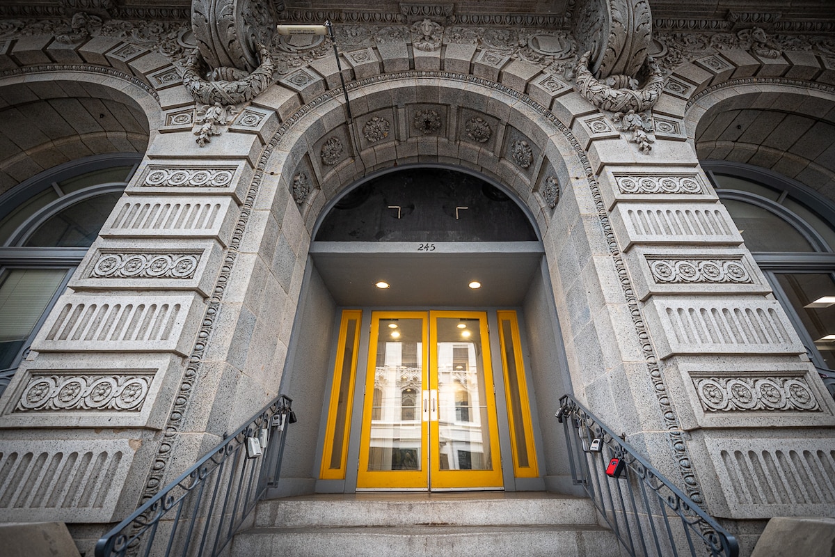 The historic building entrance is framed by intricate stonework and decorative architectural details. A pair of vibrant yellow doors serves as the focal point, flanked by well-maintained railings. Soft light is emitted from above, illuminating the entryway.