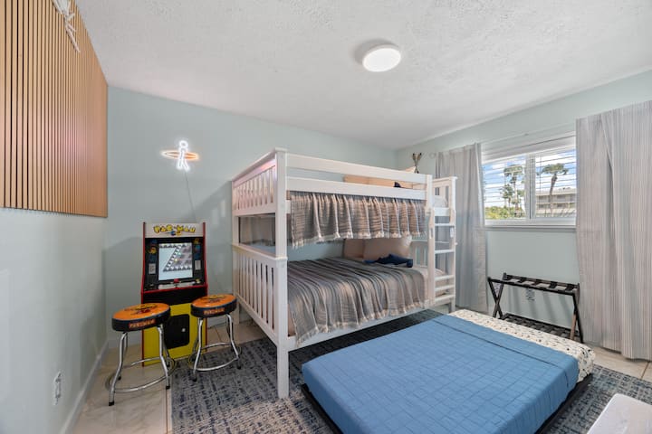 Kids room with PAC man arcade game with two stools. Top and bottom bunks are both FULL size beds and the trundle is a twin size. Closet has a dresser, hangers, spare sheets, a safety bumper for kids and two pack and plays 
