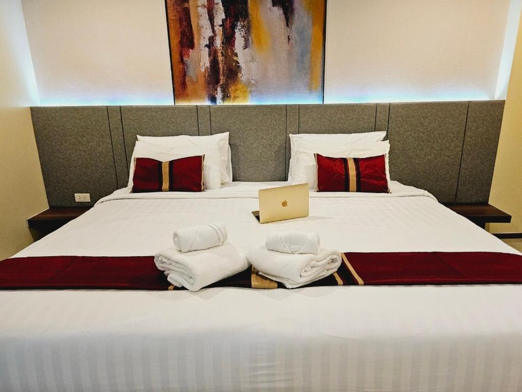 A spacious sleeping area is presented with two neatly made beds featuring soft linens and decorative cushions. A laptop rests on the bed, accompanied by neatly rolled towels. A piece of abstract wall art adds a splash of color above the headboard.
