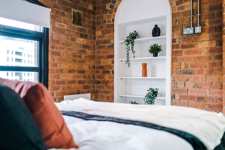 Cozy king bedroom with rich tones, exposed brick, overhead storage, and a peaceful view.