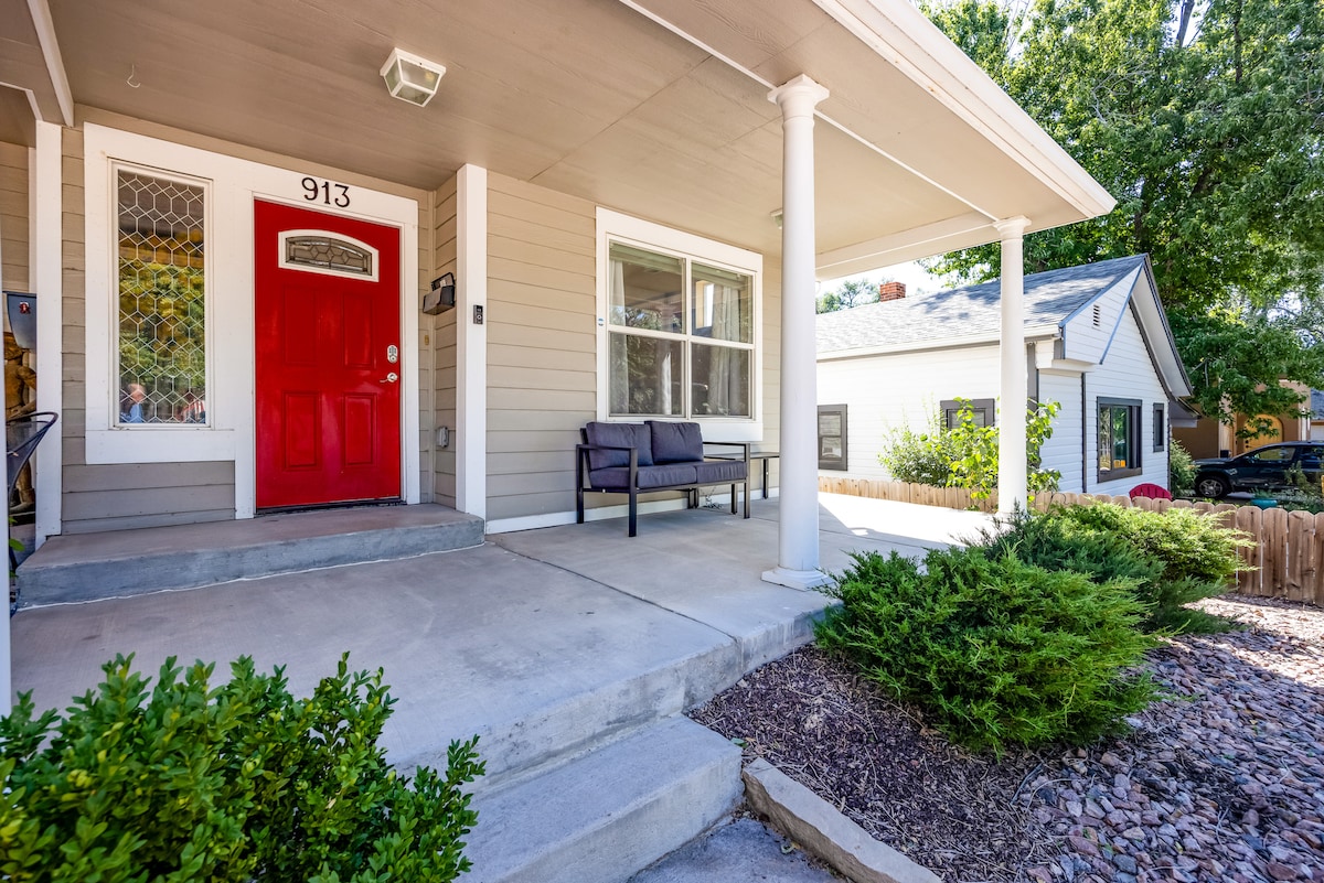 The welcoming front porch features a bold red door, enhancing the entrance. A black bench provides seating, while neatly trimmed shrubs and gravel landscaping add to the charm. The home showcases a light exterior with large windows allowing natural light.