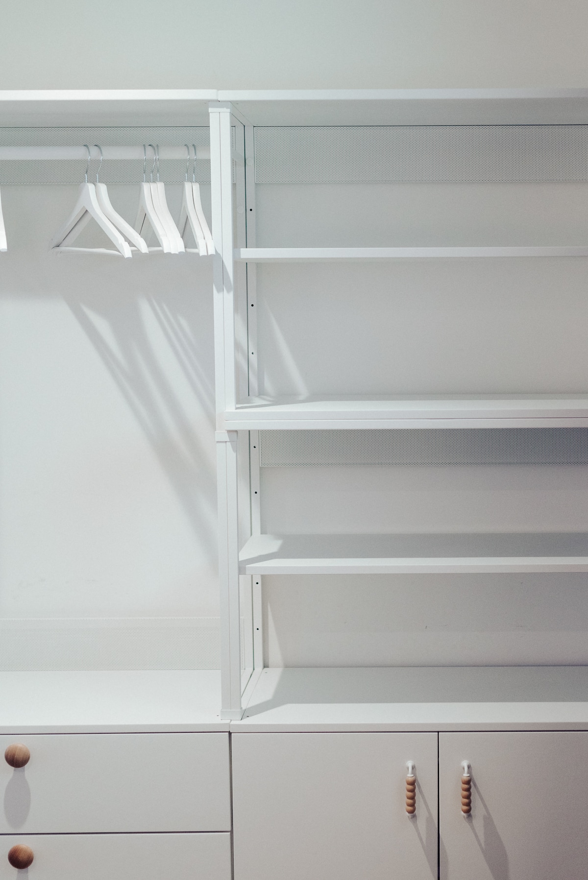 A modern closet is displayed, featuring a series of open shelves and hanging space. Several hangers are neatly arranged, while the cabinet below shows smooth white drawers with simple wooden handles, offering practical storage solutions.