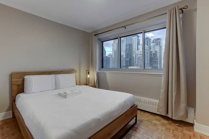 Relájate en este dormitorio sereno con una cama tamaño queen, sábanas suaves y grandes ventanales con cautivadoras vistas a la ciudad. 