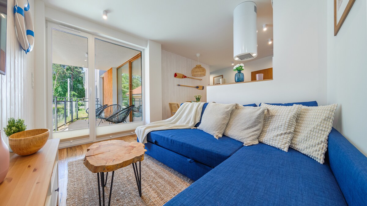 A comfortable seating area is showcased with a large blue sofa adorned with patterned pillows. A wooden coffee table with a natural finish sits in the center. Large glass doors lead to a balcony, allowing natural light to brighten the space.