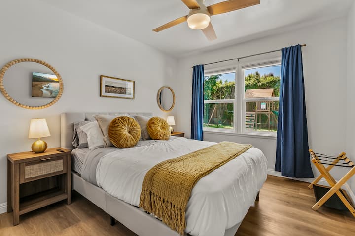 この素敵な寝室には、パリッとした白いリネンが施されたクイーンサイズのベッドがあり、快適さを高めています。濃い青色のカーテンで縁取られた大きな窓からは、自然光が部屋にたっぷり差し込み、近隣の魅力的な景色を眺めることができます。