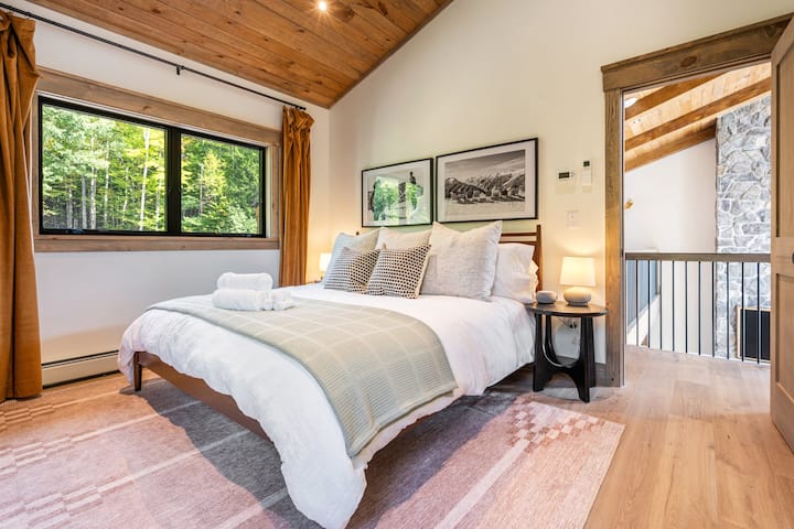 Cozy up in this inviting bedroom, featuring rustic wood accents, soft natural light, and peaceful views of the surrounding forest—a perfect retreat for relaxation after a day of mountain adventures