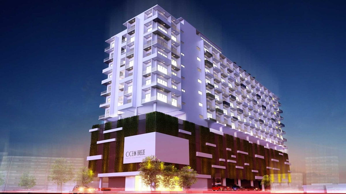 The modern building showcases a sleek design with multiple floors and large windows. Greenery adorns the lower section, contributing to the overall aesthetic. Soft lighting enhances the façade, highlighting the contemporary architecture and spacious structure.