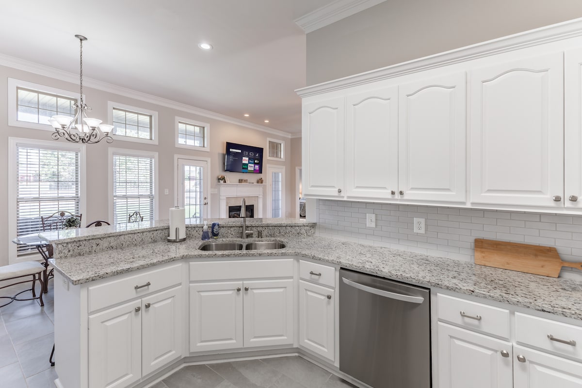 A well-equipped kitchen features white cabinetry and granite countertops, with stainless steel appliances, including a dishwasher. Natural light enters through large windows, illuminating the space. The open layout connects to the dining area, enhancing accessibility and convenience.