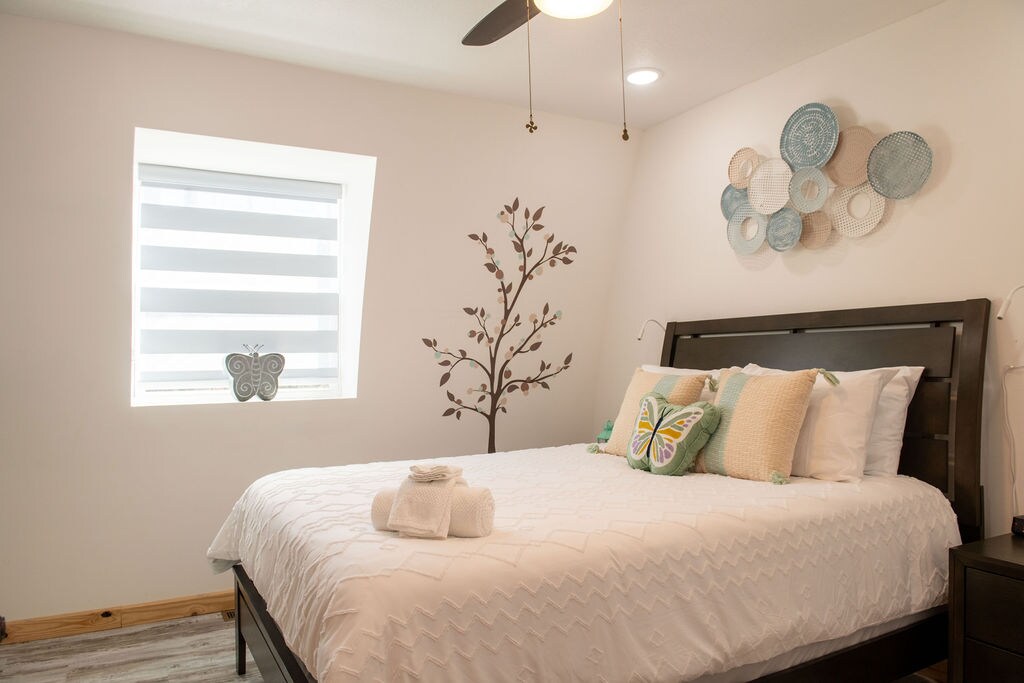 Deze serene slaapkamer beschikt over een queensize bed met zachte aqua accenten en een elegante inrichting met vlinderthema. Inclusief een dressoir, nachtkastjes en warme bedverlichting voor extra comfort.