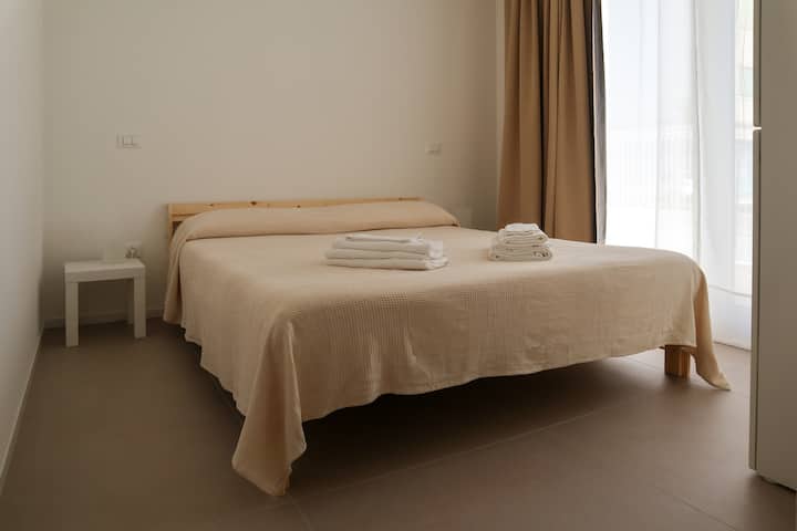 Priestor na spanie s manželskou posteľou, nočnými stolíkmi s abat jour a šatníkom s vešiakmi.