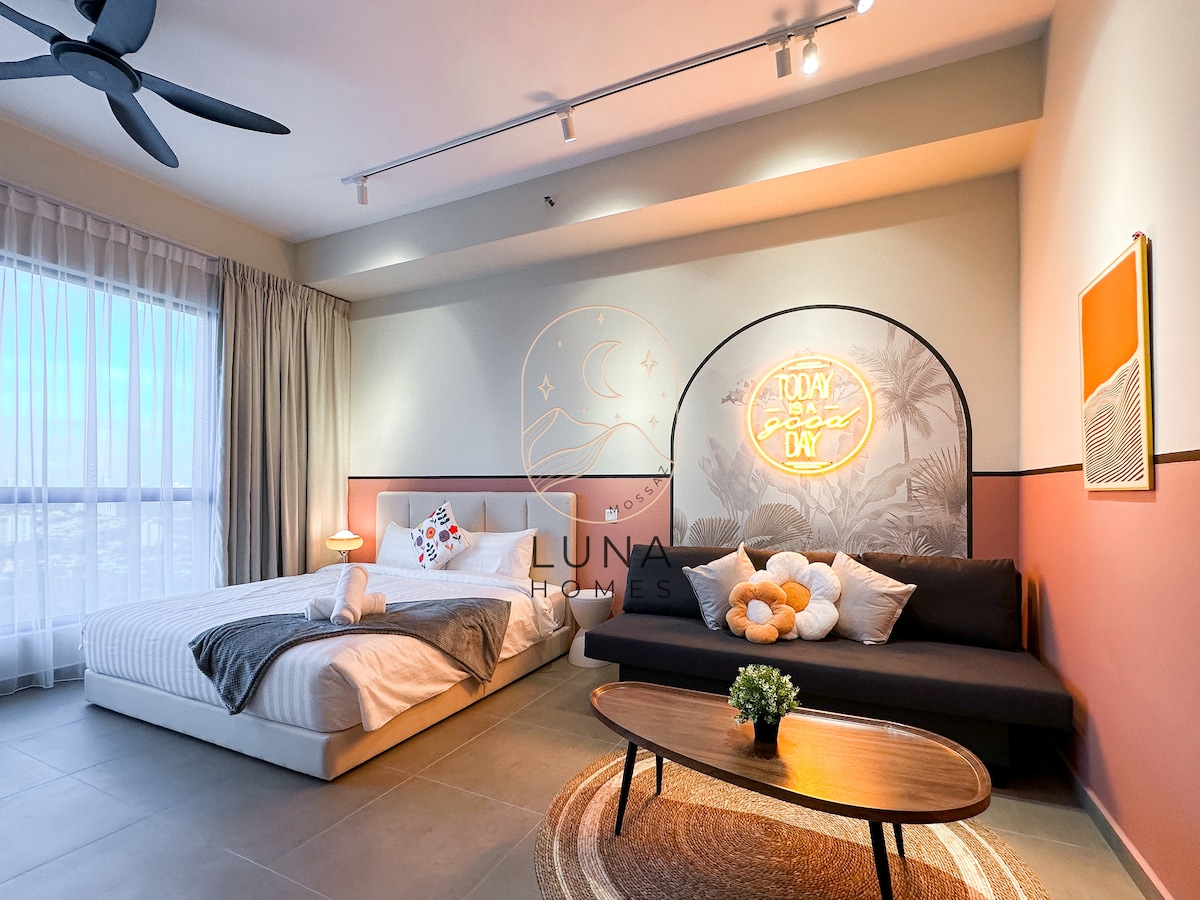 The spacious studio features a comfortable king bed with a neatly arranged quilt, complemented by a cozy sofa. Large windows invite natural light, with decorative wall art adding a subtle touch to the serene color palette.