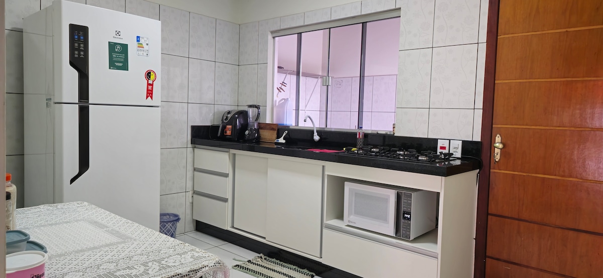 The kitchen features sleek cabinetry and a black countertop. A large refrigerator is positioned next to a gas stove. A microwave is situated below the counter. Natural light enters through a window, enhancing the space's functionality and openness.