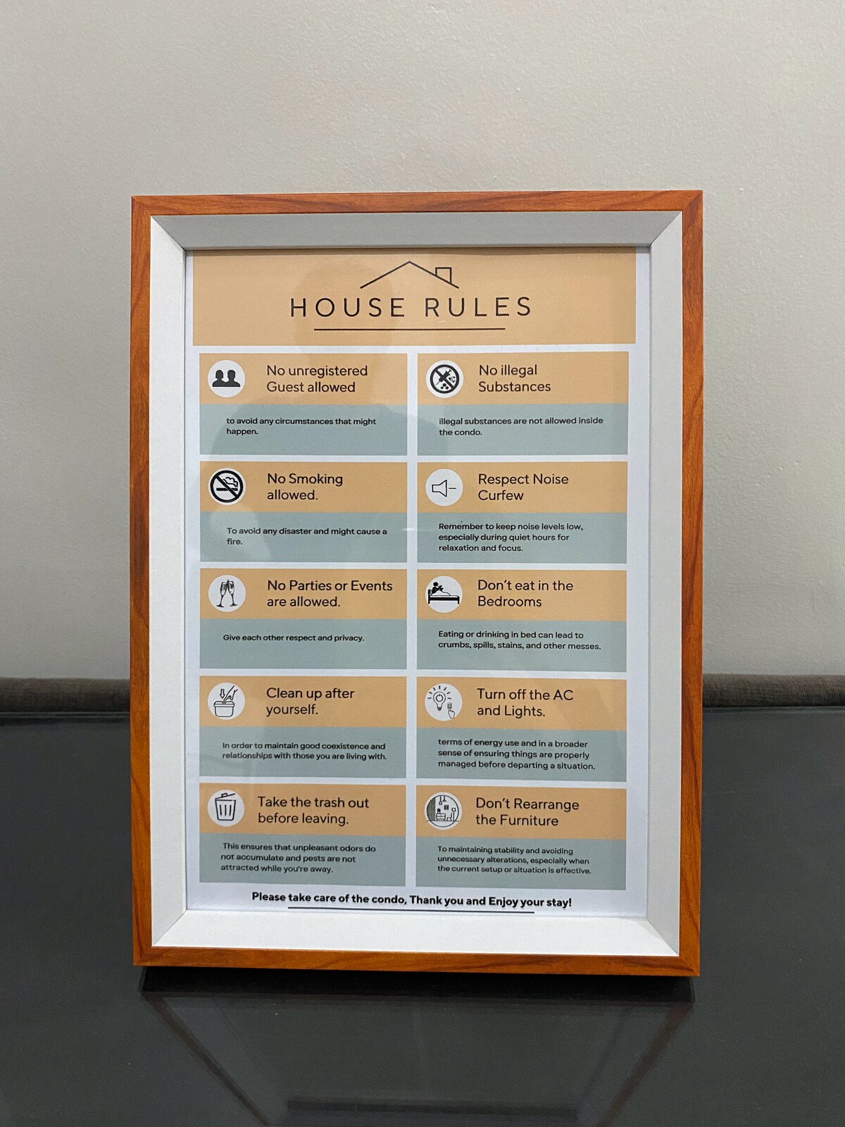 A framed sign displaying house rules is placed against a neutral wall. The rules include guidelines about guests, smoking, noise, and cleanliness, presented in clear and organized sections for easy reading.
