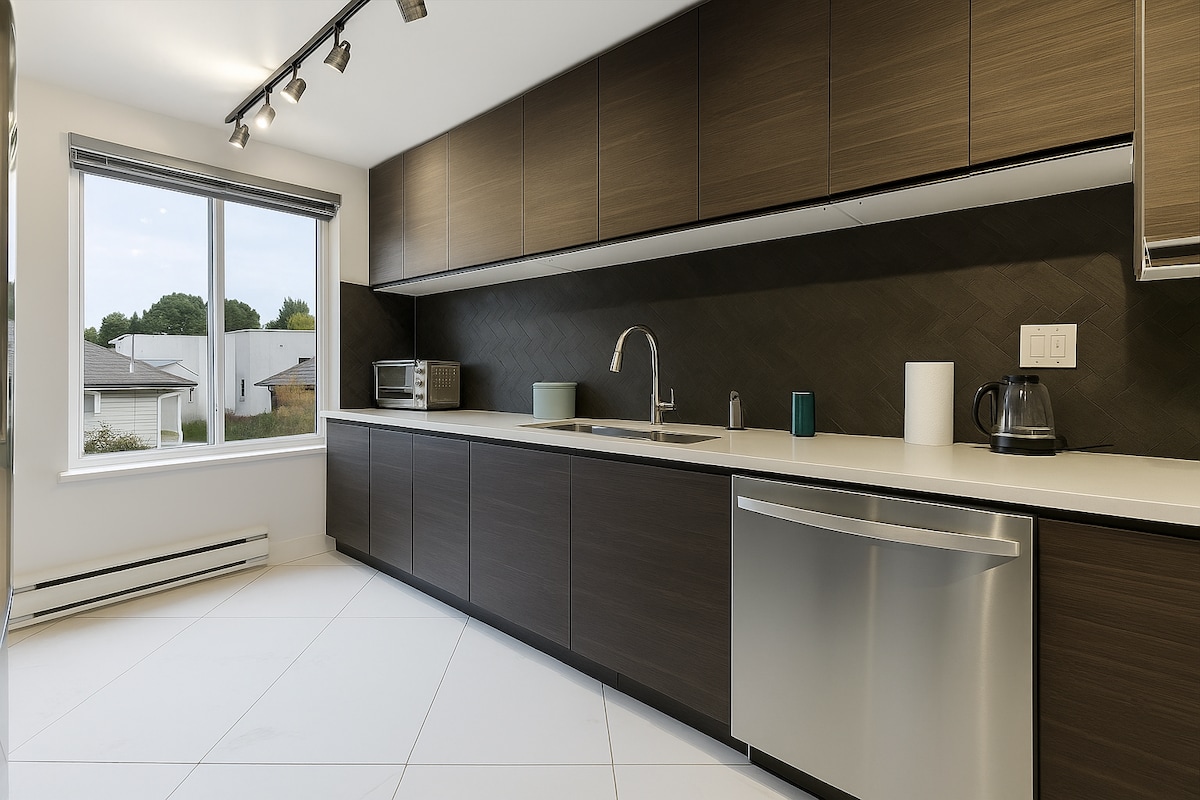 The kitchen features modern cabinetry with a sleek finish, complemented by a well-organized countertop. A large window allows natural light to illuminate the space, while essential appliances such as a microwave and kettle are clearly visible. A stainless steel dishwasher adds to the functional design.