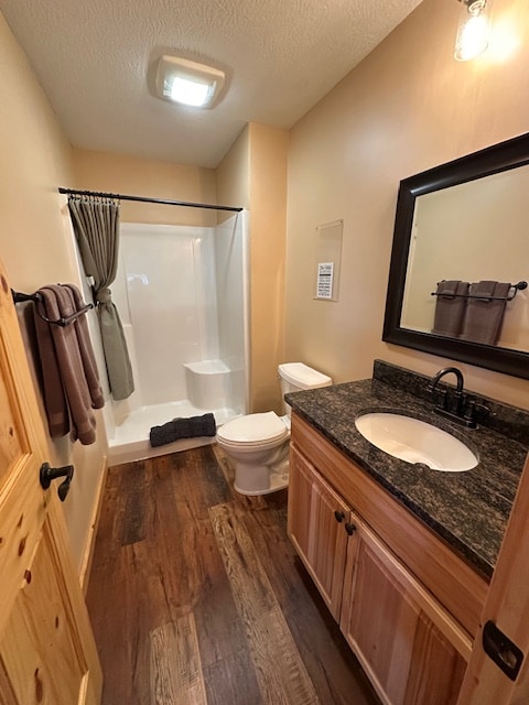 A well-lit bathroom is presented, featuring a walk-in shower with a clear glass door. A toilet and a single sink with a dark countertop are included. Warm wooden cabinetry and flooring create a natural aesthetic, complemented by neutral wall tones and a decorative mirror.