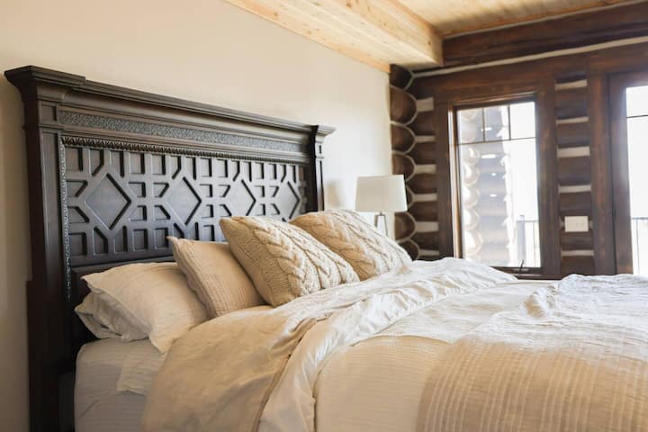 Rilassati in questa lussuosa camera da letto con letto king size, testiera splendidamente intagliata, morbidi cuscini in maglia e lenzuola soffici a strati. Circondato da tonalità di legno naturale e accoglienti texture da baita, è il tuo rifugio tranquillo dopo una giornata nella natura.