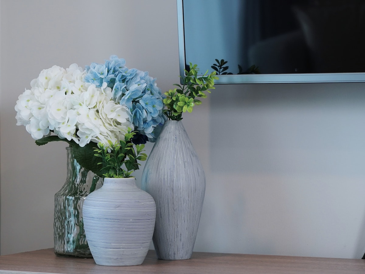 A collection of decorative vases is displayed on a surface, featuring blue and white flowers alongside greenery. The vases vary in shape and texture, complementing the modern decor and providing a touch of natural beauty to the living space.