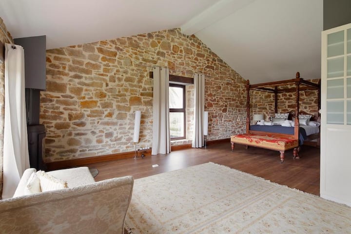 Großes Hauptschlafzimmer mit einem 150 cm großen Bett, einem Einzelkamin, einem komfortablen Schreibtisch für mobiles Arbeiten und einem eigenen WC. Blick auf die geräumige Wiese des Hauses.