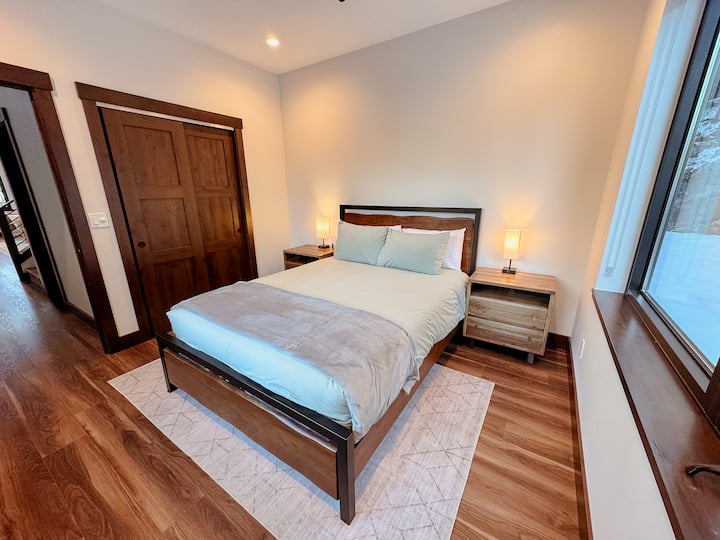 Chambre confortable avec un lit Queen, entourée de fenêtres pour une retraite paisible et inspirée de la nature.