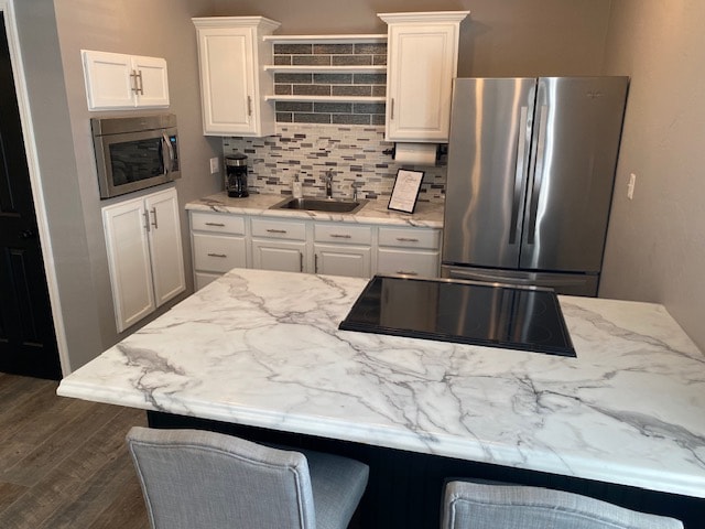 The kitchen features sleek white cabinets and a marble countertop, complemented by a tile backsplash in muted shades. An island with seating is positioned at the center, while modern appliances, including a stainless steel refrigerator and microwave, are visible along the wall.