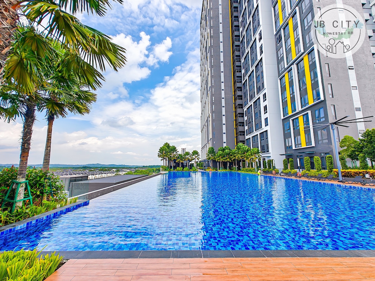 The rooftop infinity pool is surrounded by palm trees and lounge chairs. Its calm blue waters reflect the sky and nearby greenery, creating a serene environment. The high-rise building looms elegantly in the background, enhancing the tranquil atmosphere of the space.