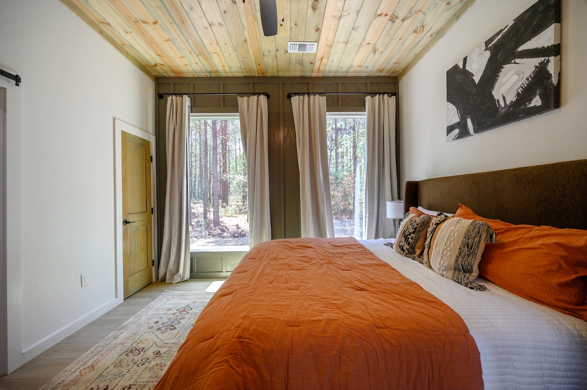 Acogedor dormitorio con tonos cálidos, techo de madera, vistas al bosque y arte moderno, perfecto para un relajante refugio en una cabaña.
