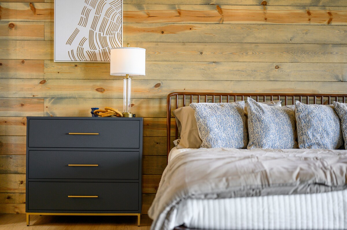 Dormitorio moderno con pared decorativa de madera, cojines azules y elegante mesita de noche con lámpara.