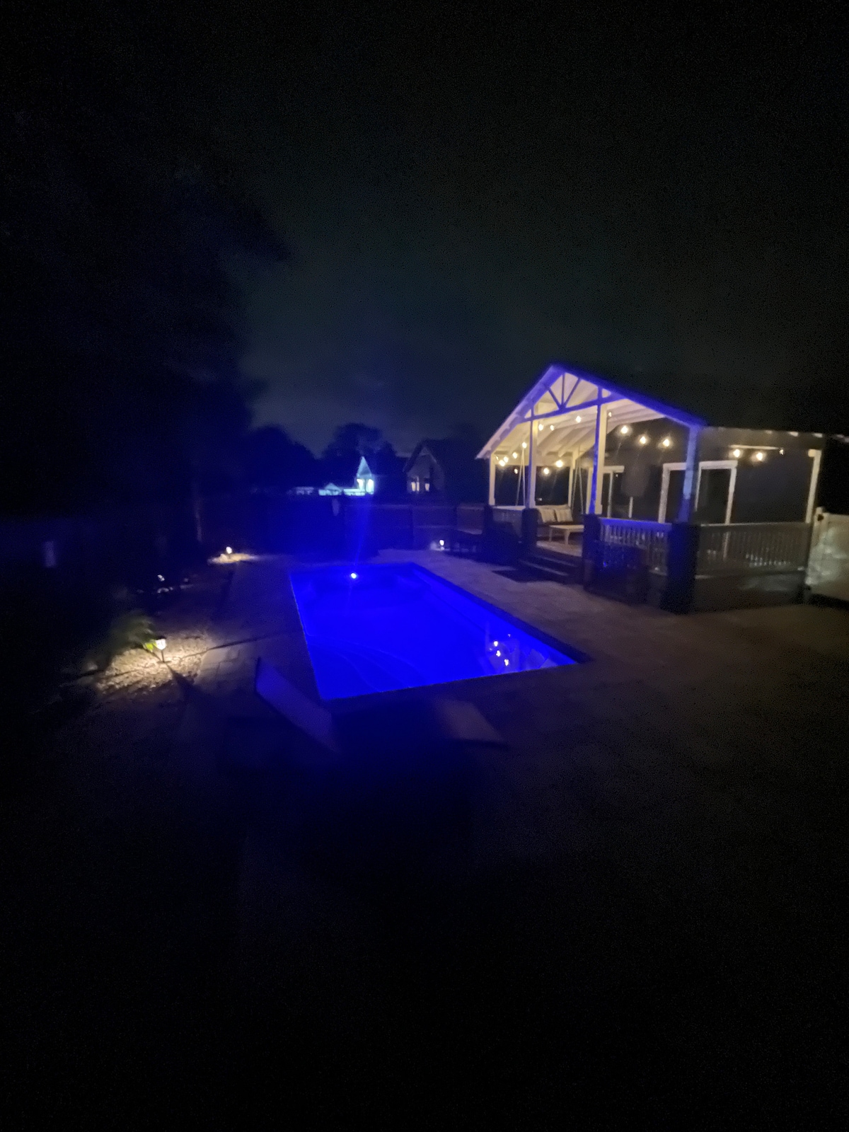 A serene outdoor space is featured at night, showcasing a solar heated pool illuminated in a calming blue hue. A cozy covered patio is visible in the background, with soft lighting creating a warm ambiance, enhancing the peaceful atmosphere.
