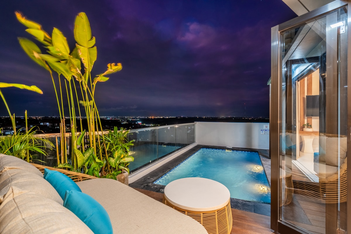 A serene terrace features a private pool surrounded by lush greenery and stylish outdoor furniture. The evening sky is adorned with soft purple hues, enhancing the tranquil ambiance. Visible reflections of the landscape can be seen in the pool water, emphasizing the connection to nature.