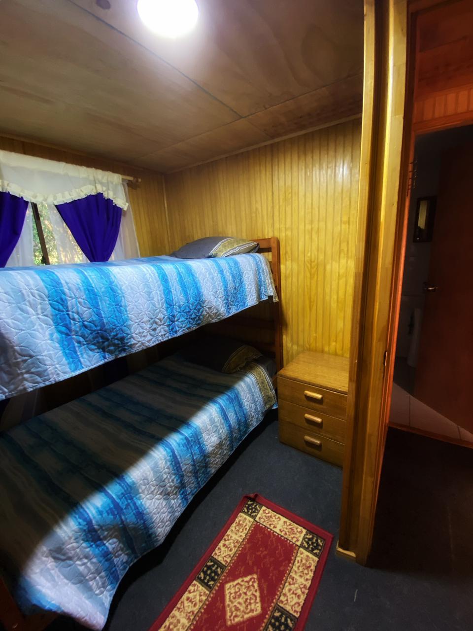 Camarote o litera con sabanas, frazadas y cobertor ya dispuestos, listos para ser utilizadas. un velador y un estanque para guardar ropa.