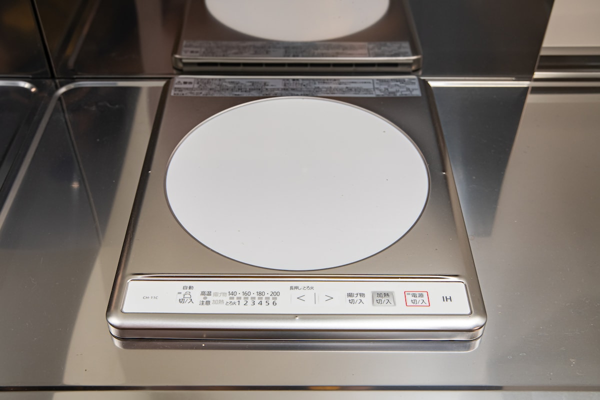 An induction cooktop is displayed on a sleek stainless steel countertop. The interface features clear control buttons for adjusting heat settings, providing a modern cooking experience.