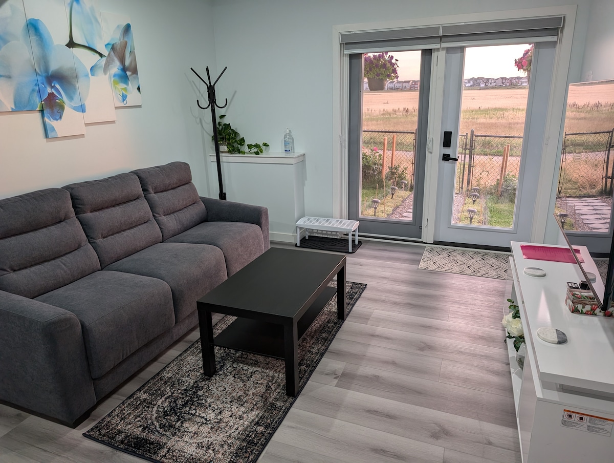 A modern living area features a gray sectional sofa positioned adjacent to a black coffee table. Natural light enters through sliding glass doors, offering views of an outdoor area. Decorative artwork hangs on the walls, complementing the light-colored flooring.