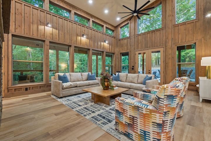 Прекрасен главен дневен простор со двостран камин, маса за покер и дрвени детали низ надворешноста. 