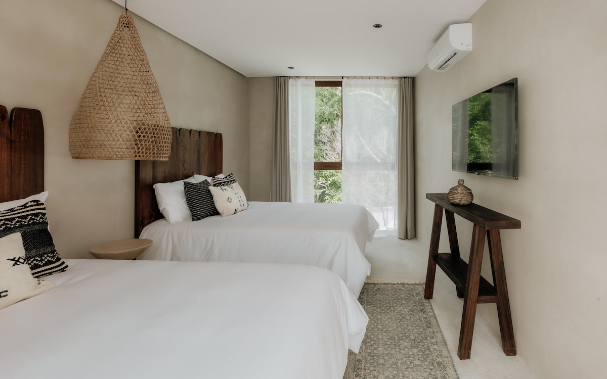 The third bedroom features twin queen beds, a wall-mounted TV, and a large window overlooking the pool and jungle.