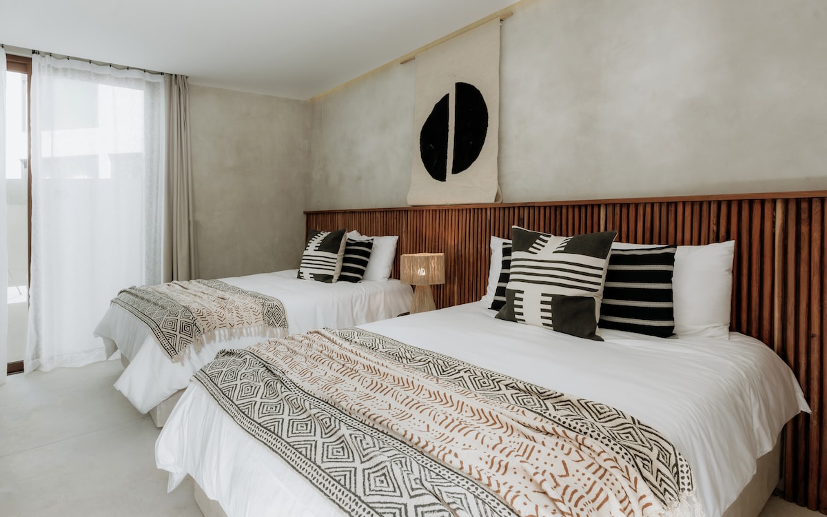Bedroom five features twin queen beds, a tropical wood dual headboard, and hand-picked black and white design elements for a pleasant and harmonious space.