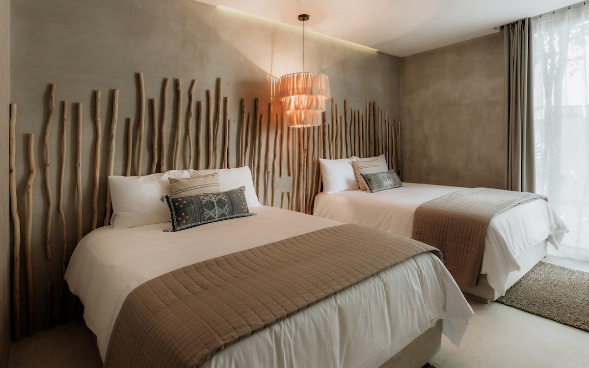 The fourth bedroom, located on the ground floor, features twin queen beds and an en-suite bathroom. Playfully designed with tropical wood and handcrafted elements.