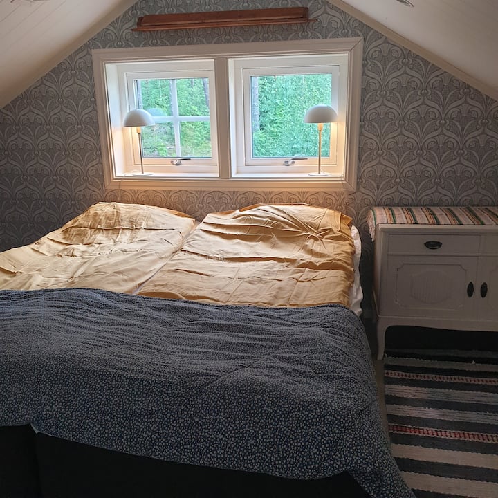 غرفة نوم علوية مع سرير مزدوج وسرير مفرد، وسرير مفرد تحت سقف مائل. درج حلزوني يصل إلى الشقة العلوية.