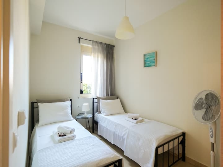 Um quarto de solteiro bem iluminado e convidativo, com duas camas confortáveis, lençóis limpos e uma decoração minimalista. A grande janela permite que a luz natural flua, criando um ambiente relaxante e arejado.