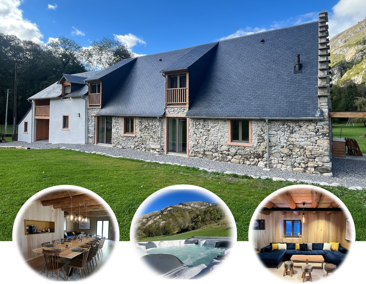 The exterior of the gîte displays a combination of stone and wooden elements, with a steeply pitched roof and large windows inviting natural light. A well-maintained grassy area surrounds the building, creating a spacious and open environment. The backdrop features gentle hills and trees, enhancing the serene setting.