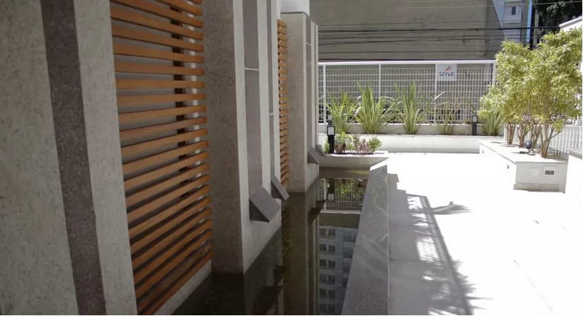 A serene outdoor space is presented, featuring a sleek water feature reflecting the surrounding greenery. Vertical wooden panels offer a sense of privacy while soft light enhances the minimalistic design. Lush plants line the area, contributing to an inviting atmosphere.