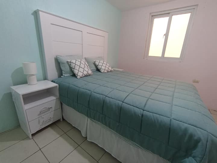 Recámara secundaria ubicada en el segundo nivel con sus dos mesas de noche, una lámpara de noche y su cabecera. Habitación iluminada y cuenta con su cortina.