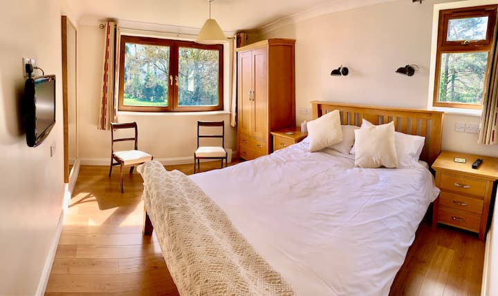 Cama tamaño king, mesitas de noche, sillas y armario con bañera y ducha adyacentes