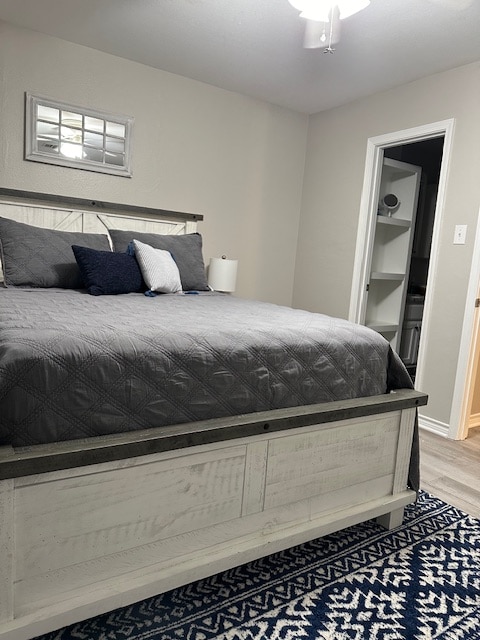 A spacious bedroom features a large bed dressed in gray bedding, accented with decorative pillows. A contrasting area rug adds texture to the space. There is a closet visible in the background, along with a small window above the headboard allowing natural light.