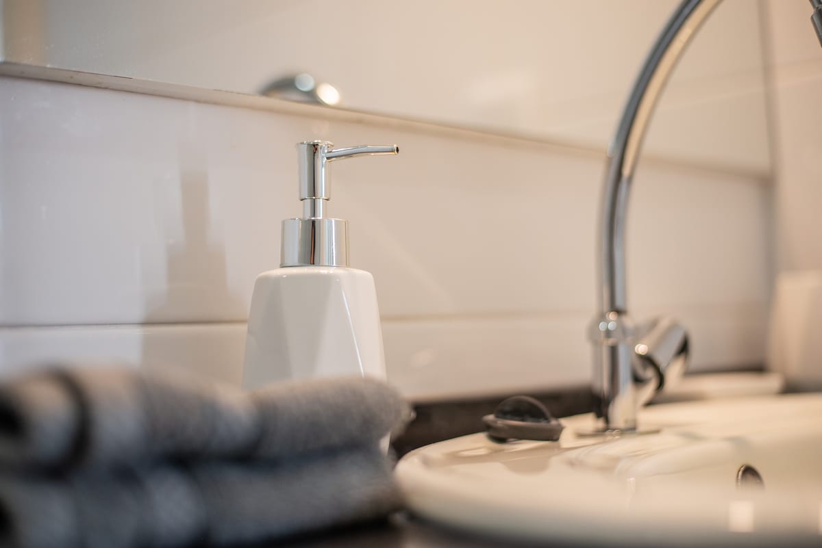 The image features a modern bathroom sink area, showcasing a sleek faucet and a minimalist soap dispenser. A neatly folded grey towel is positioned beside the sink, which is set against a backdrop of light-colored tiles, enhancing the clean and tidy appearance.