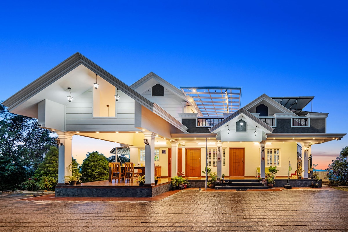 The exterior of Titha Villa is showcased at twilight, highlighting its charming architectural design. The entrance features well-lit pathways, a spacious balcony, and large windows. Surrounding greenery enhances the serene setting, contributing to a welcoming arrival experience.