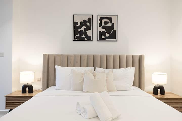 Chumba cha kulala chenye starehe kilicho na kitanda kikubwa, starehe nyeupe na mito iliyopangwa vizuri. 