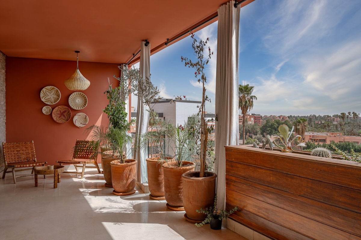 A spacious terrace features decorative planters brimming with greenery, enhancing the outdoor space. Comfortable seating arrangements are visible, along with elegant light fixtures. Large windows allow natural light and offer unobstructed views of the surrounding scenery.