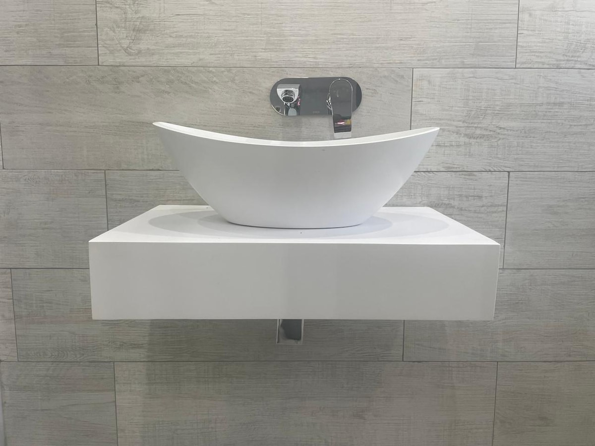 A stylish bathroom sink is positioned on a wall-mounted shelf. The sink features a sleek, modern design with a curved shape, and is complemented by a contemporary faucet. The light-colored tiles in the background enhance the clean and minimalistic feel of the space.